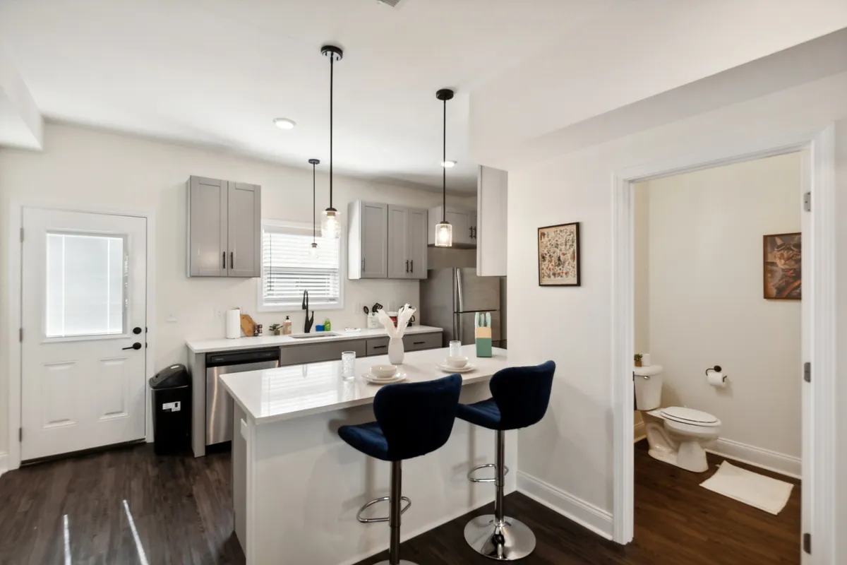 A contemporary kitchen featuring a central island with bar stools, modern appliances, and decorative artwork on the wall. The space is staged for cooking, entertaining, and casual dining, with ample surfaces for meal prep and socializing.