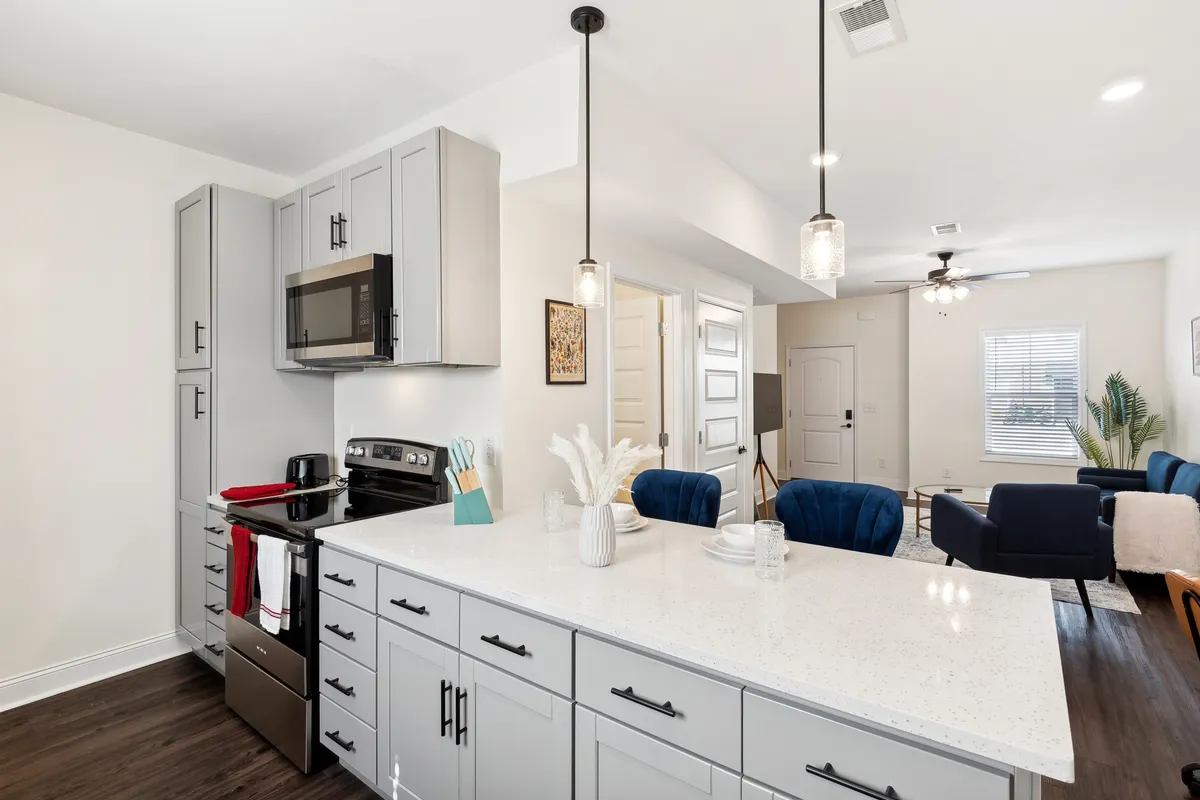 A stylish kitchen island with bar stools, modern appliances, decorative wall art, and a glimpse into the living room. The layout is open and welcoming, suitable for everything from family meals to entertaining guests. The connection between kitchen and living area is visually clear.