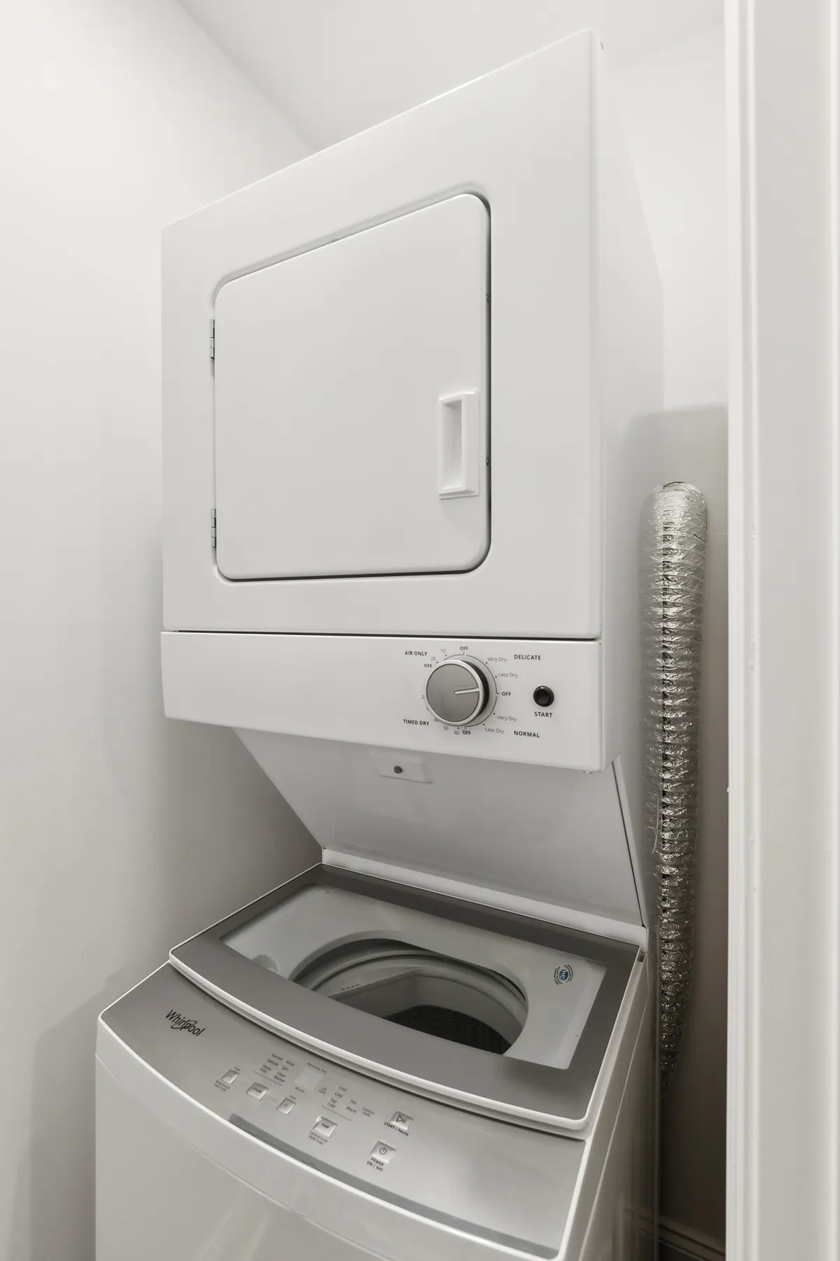 A practical laundry nook with a stacked washer and dryer, complete with a modern control panel and organized vent tubing. The setting is tidy and efficient, emphasizing ease of use for everyday living.
