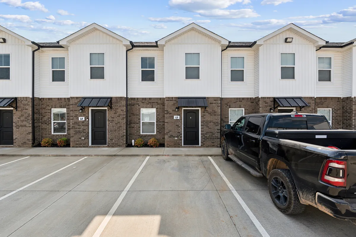 This image showcases the townhouse's welcoming exterior facade, with inviting landscaping elements and a vehicle parked in the foreground. There are hints of social activity, such as children playing and neighbors chatting, which contribute to a lively community vibe ideal for families.