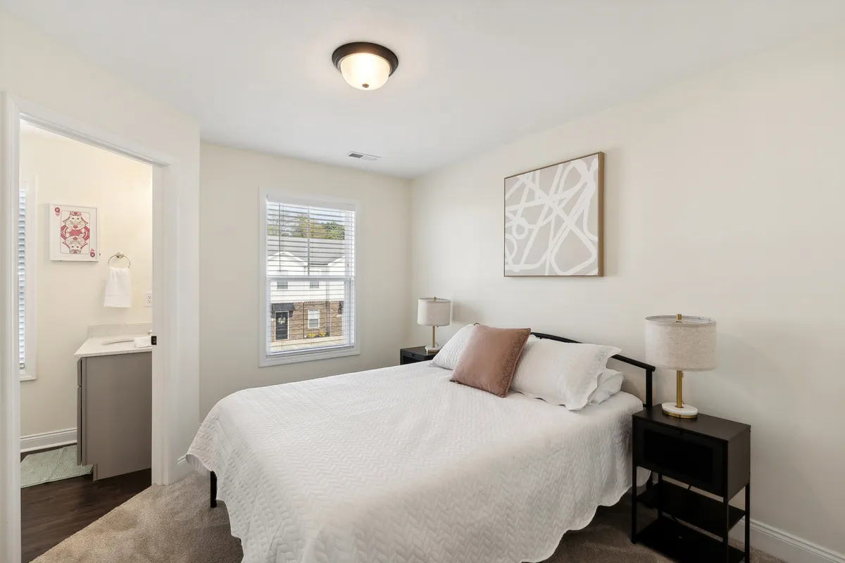 A peaceful bedroom with a comfortable bed, artwork on the wall, nightstands with lamps, and a window that allows in natural daylight. The mood is peaceful and inviting, emphasizing relaxation and privacy.