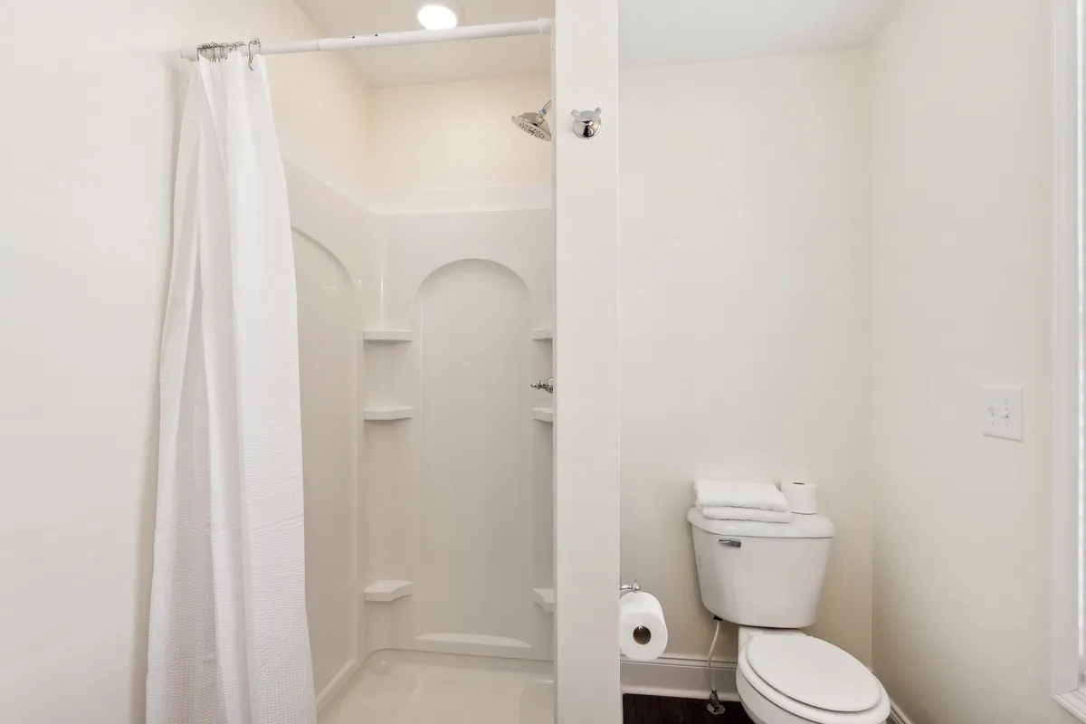 A modern bathroom setup with a shower area, towels neatly arranged, and a toilet. The space feels serene and refreshingly clean, emphasizing convenience and a touch of luxury for guests.